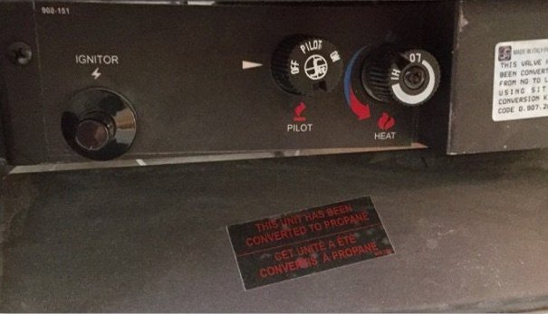 Close-up of the fireplace gas controls: an ignitor button, a gas control knob marked OFF and PILOT, a heat dial, and a red label below saying the unit has been converted to propane.
