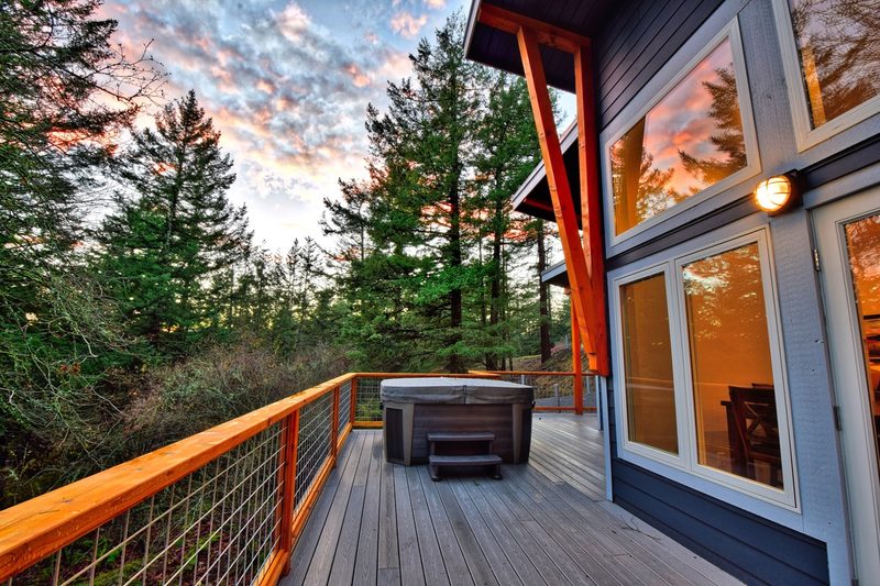 The hot tub on the main living deck at Rosario, cover on, with a table and chairs and trees beyond the railing.